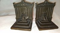 Pair of antique bronze bookends, classical temple design with columns and detailed pediment, showing front view of both pieces side by side on white surface.