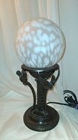 Full view of Gothic style lamp showing mottled white glass globe and metal base with winged creatures.
