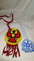 Front view of both Indigenous hand beaded necklaces on fabric background showing thunderbird eagle designs and colors.