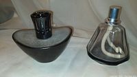 Two Lampe Berger aroma diffusers, one black-grey ceramic and one clear glass, shown assembled with removable tops.