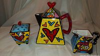 Front view of teapot, sugar bowl and creamer showing multicolor patchwork pop art design with hearts and geometric patterns.