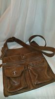 Brown leather Roots messenger bag front view showing front zippered and flap pockets with turn-lock closure and adjustable strap.