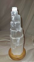 Single selenite tower light with USB cord attached, showing the translucent crystal structure and wooden base.