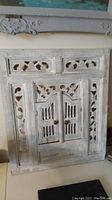 Front view showing the carved white painted teak wood frame with closed shutters over the mirror.