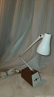 Front view of the vintage small industrial desk lamp standing upright with adjustable white arm and conical lampshade on brown rectangular base with two switches.