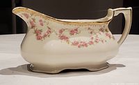 Side view of the creamer showing pink rose floral garland, gold rim detailing, and ornate handle