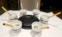 Image showing the entire serving set with six porcelain bowls each containing a spoon, arranged around the black metal spinning tray.