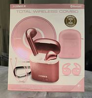 Photo of the full box showing rose gold true wireless earphones, charging case, wireless charging pad, pink case cover, earphone neck strap, secure fit earpieces, and black carabiner.