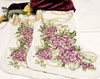 Two large Christmas stockings with white body showing purple hydrangea floral print, beige rope designs, and burgundy velvet fold-over top with gold tassel, laid flat.