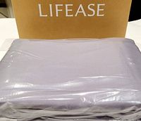 Lifease brown packaging bag behind a folded purple fabric bundle sealed in clear plastic showing front folded view.