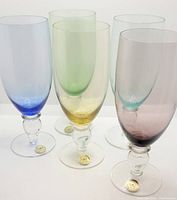 Five large mouth blown crystal goblets in pastel colors with gold foil stickers on the base.