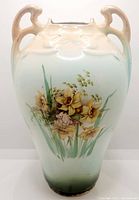 Front view of antique ceramic vase showing color gradient and floral daffodil painting with two handles.
