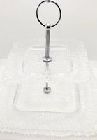 Front view showing the assembled two-tier serving tray with top and bottom square plates and central metal handle.