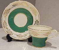 Front view of tea cup and saucer showing green band with gold leaf pattern on cream background