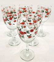 Front and angled view of six clear glass goblets decorated with red poinsettia flowers and green leaves on the upper portion of each glass.
