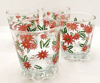 Four clear glass tumblers decorated with red poinsettia flowers and green leaves, shown grouped together.