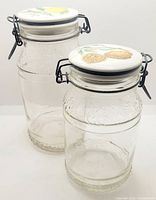 Front angled view of two glass canisters showing lemon and walnut ceramic lids with locking metal clasps.