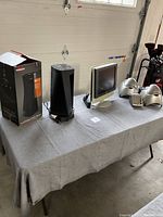 Full view of the table with a black Vornado heater next to its original box, Sony flat screen TV, and multiple silver Sharper Image speakers arranged on gray cloth.