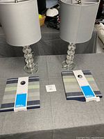 Two crystal lamps with stacked spherical bases on a gray tablecloth with two rectangular striped fabric storage bins in front.