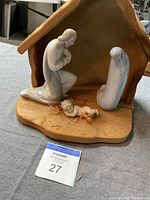 Porcelain nativity set with wooden crèche showing Jesus, Mary, and Joseph figurines inside the stable