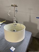 Full view of the pendant light showing ivory drum shade and metal canopy with hanging rod.