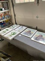 Six framed prints on a table including botanical and artistic portrait themes, showing overall lot contents