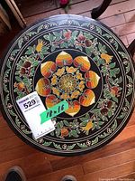 Top view of the round Asian lacquered table showing detailed colorful floral and fruit designs in yellow, orange, green and red on a black background.