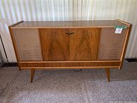 Full front view showing wooden console, woven speaker grilles, central door and tapered legs