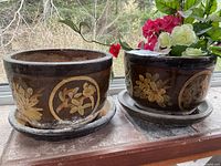 Two planters side by side on windowsill, one holding faux flowers, both on matching saucers