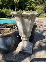 Front view of one white marble urn showing fluted panels and scalloped rim above pedestal base.