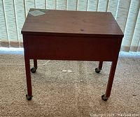Full side and front view of a small teak sewing table on caster wheels.