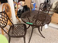 Full view of round aluminum table with lattice pattern and two matching chairs.
