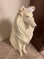 Front view of a large ceramic dog figurine sitting on carpet against wall.
