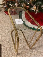 Angled front view of brass side table with glass top showing gold trim and curved legs.