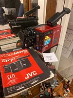 Photo of the JVC VideoMovie GR-C7U video camera with instruction manual positioned next to it on a glass shelf.
