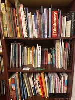 Photo of top three shelves of the wooden bookshelf filled with a diverse collection of books.
