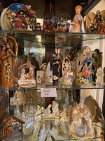 Glass cabinet shelf showing a variety of religious statues and nativity scenes, including stained glass decor, ceramic figures, and a candle holder.