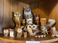 Display of multiple wooden owl decor pieces on wooden shelf, various sizes and styles