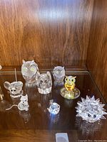 Overall view of 8 Swarovski crystal animal figurines arranged on a shelf against a wood backdrop.