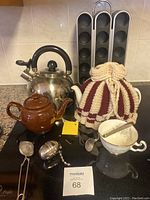 Photo showing kettle, brown ceramic teapot, white teapot with crochet cozy, sugar bowl with spoon, metal tea infuser, and tea leaf strainer with Mindreader Pod dispenser in background