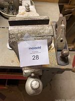 Top down view of the large Parker J242 bench vice with metal jaws and screw handle, showing wear and a MaxSold lot number tag attached on top.