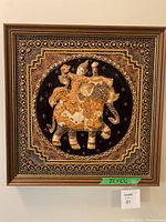 Full view of framed wall decor with an elephant carrying a rider in detailed textured fabric and embellishments.