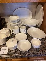 Set of white Johnson Brothers Apollo dishes arranged showing plates, bowls, mugs, butter dish, creamer, and sugar bowl with ribbed vertical line design.