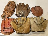 Top view of six antique leather baseball gloves in varying styles and colors laid flat on table