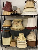 Photo showing the full assortment of lampshades on a storage rack, varied shapes, colors, and materials.