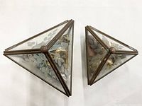 Top-down view of two glass terrarium style jewelry boxes, filled with assorted jewelry, showing their pyramid shape and bronze metal frames with etched leaf decoration.