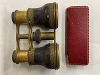 Top-down photo of the vintage opera glasses with brass and black parts next to their red leather case