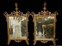 Pair of tall antique mirrors side by side with ornate gilded frames and detailed scroll and leaf carvings, showing wear and damage to frame.