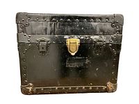 Front view of small black metal steamer trunk showing brass lock and two side latches with riveted metal framing.