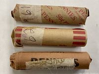 Three paper rolls containing pennies from the 1960s; each roll is labeled with a year (1960 S, 1962, 1961). The rolls have distinct paper wrappers and appear aged.